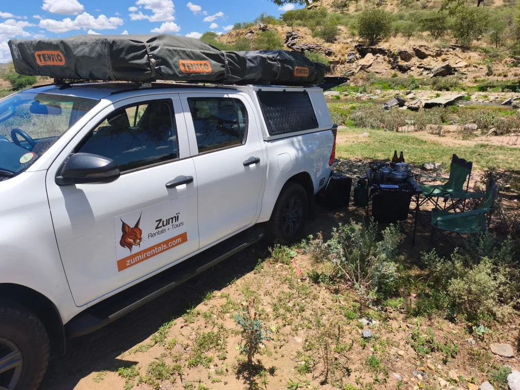 Zumi Toyota Hilux with rooftop tents and camping equipment set up beside a river in Namibia